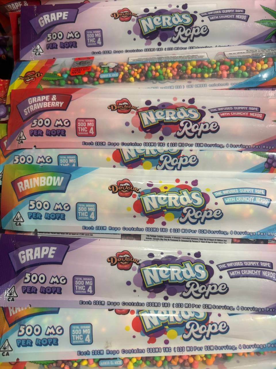 Stacked packages of Devour brand 500mg THC infused gummy Nerds Rope candy in various flavors.