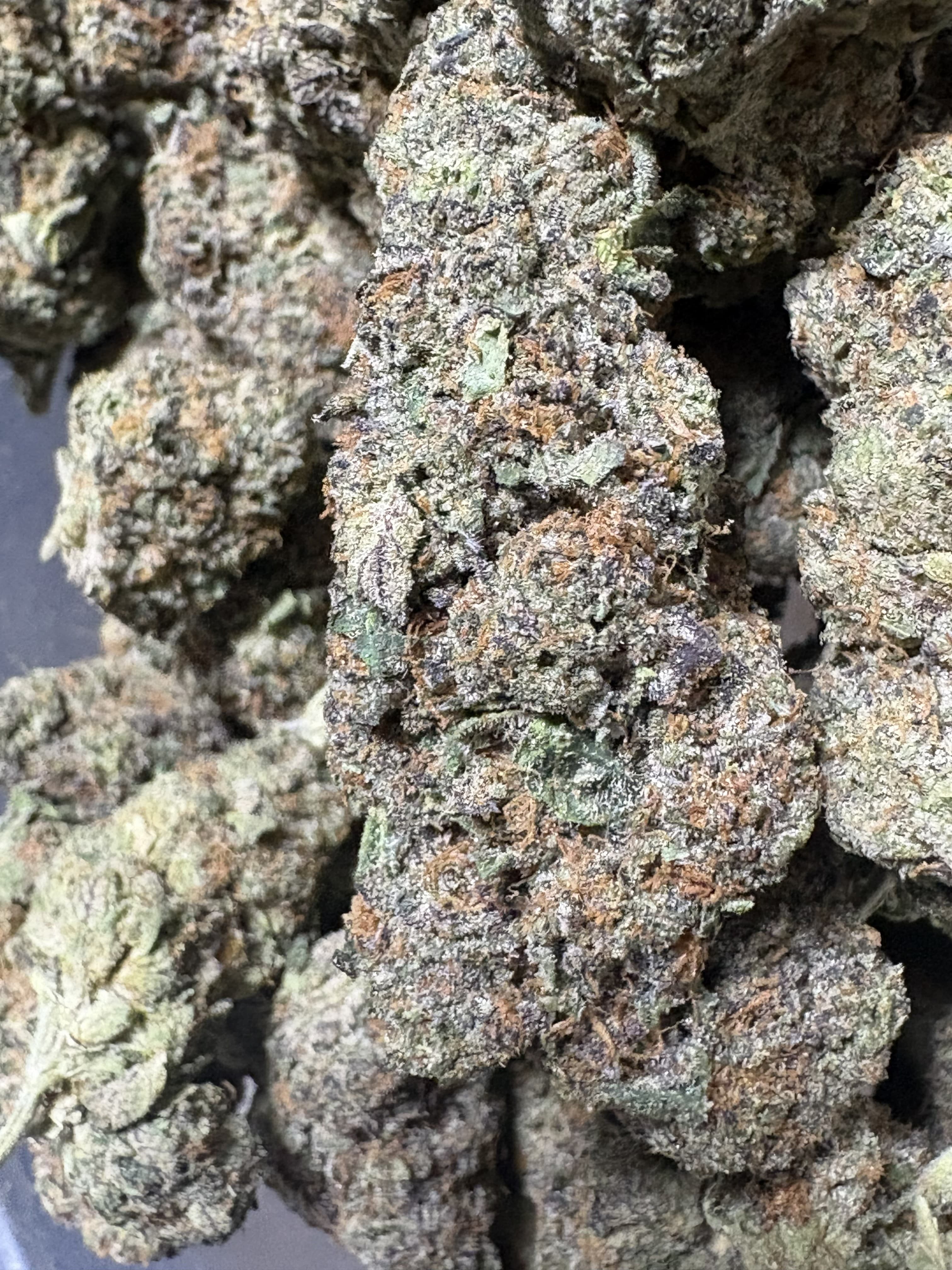 Dense, frosty cannabis buds showing a mix of green and purple colors with orange pistils.